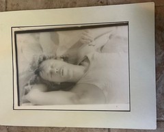 black and white photograph of Paul Thek in undershirt lying down eating an Orio